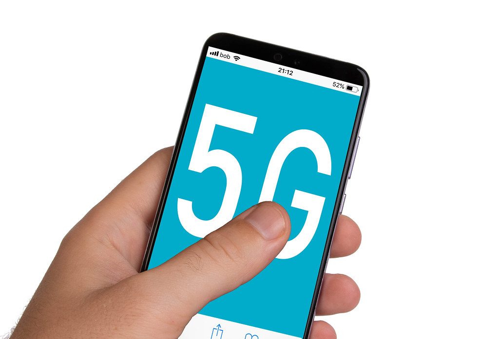 ブルースクリーンに5Gテキストを備えたスマートフォンを保持している男性の手
